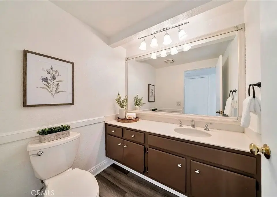 Bathroom with large mirror, sink, dark wood cabinets, plant on counter, toilet, and towels.