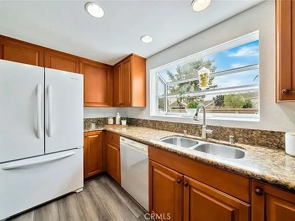 Kitchen with wooden cabinets, white fridge, sink under window, and granite counter.