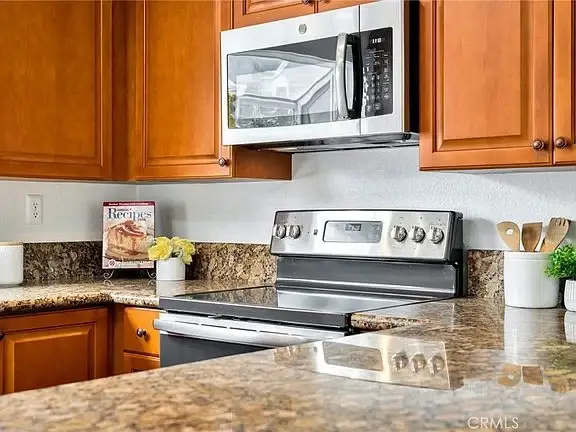 Kitchen with wooden cabinets, microwave above stove, stainless oven, and granite counter.