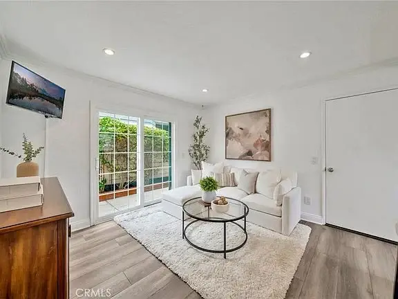 Living room with white sofa, glass coffee table, wall art, light rug, and sliding glass doors.
