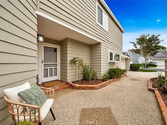 Pathway to house California real estate with beige siding, small seating area with pillows, plants