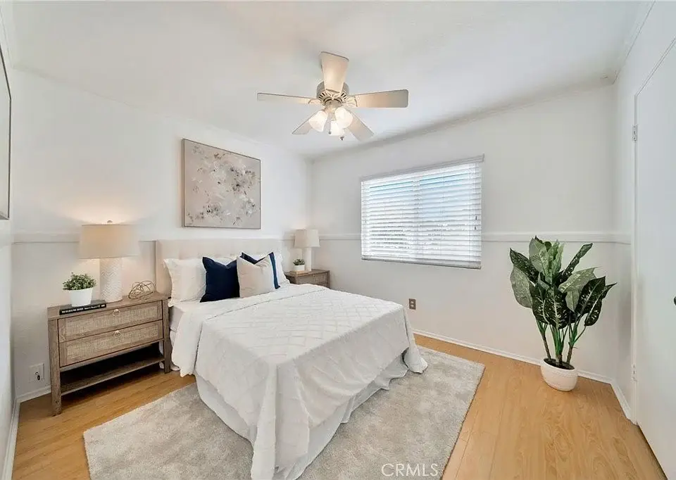 bedroom with white bedspread, side tables with lamps, window with blinds, and a plant.