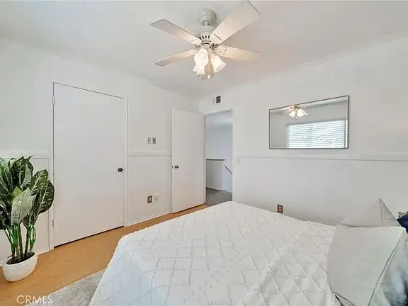 bedroom with white walls, bed, mirror, ceiling fan, plant, and open door to another room.