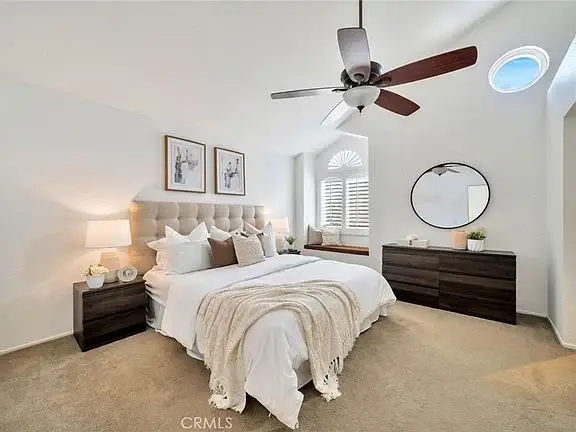 bedroom with headboard, pillows, lamps, dresser, and big windows with shutters.