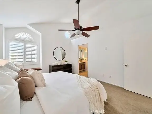 bedroom with large bed, pillows, dresser, mirror, ceiling fan, and window with shutters.