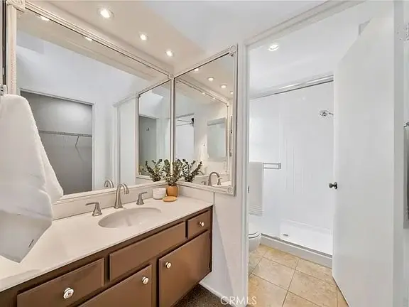 Bathroom with double sink, brown cabinets, big mirrors, and walk-in shower.