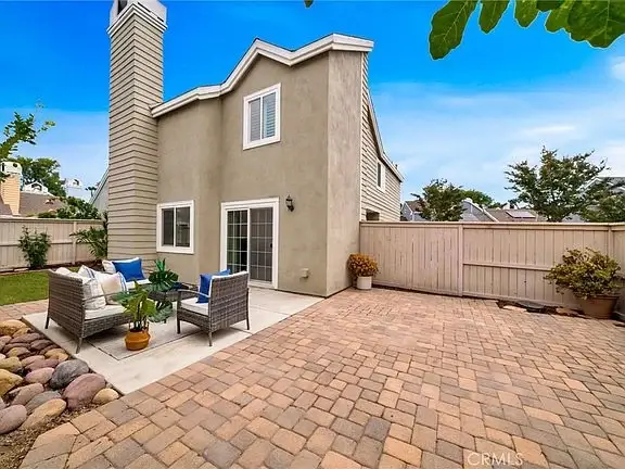Back patio of house California real estate with brick floor, chairs with cushions, and green yard.