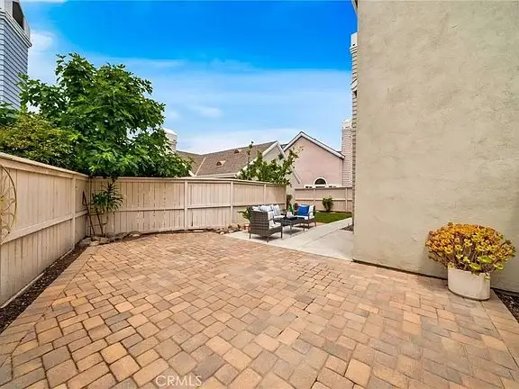 Outdoor patio with paved floor, plants, low fence, and outdoor furniture under blue sky.