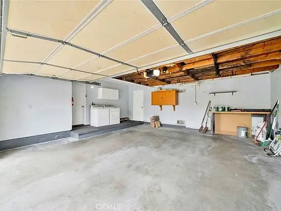 Spacious garage with concrete floor, workbench, cabinets, and tools on the wall.