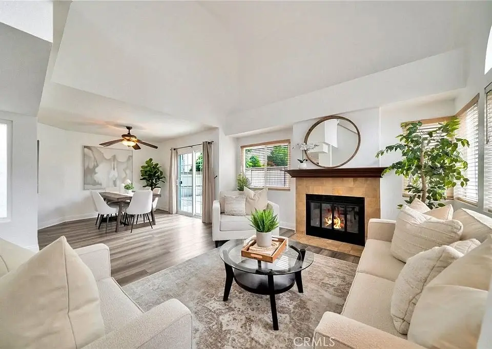 Living room with fireplace, round mirror, coffee table with plants, cozy seating, and dining area in back.