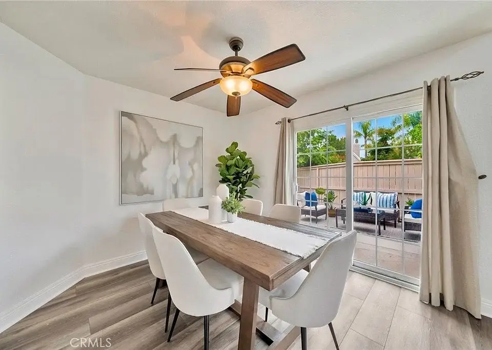 dining area with wooden table, white chairs, ceiling fan, sliding glass doors, and a plant.