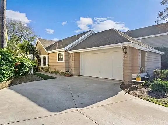 Single-story house, California real estate, with beige siding, two-car garage, and driveway with greenery