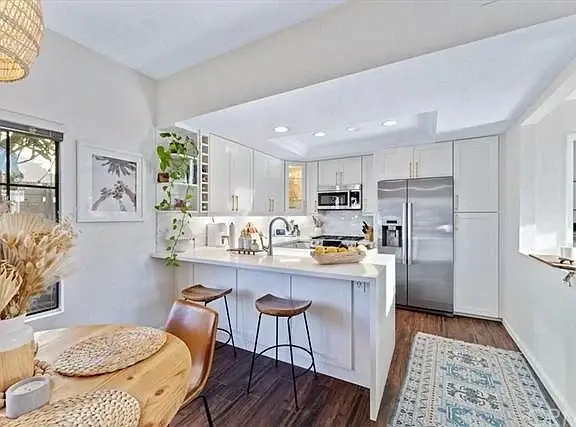Kitchen with white cabinets, stainless steel appliances, small island with seating, dining table, and plants
