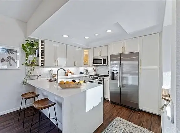 Kitchen with white cabinets, stainless steel appliances, large island with seating, and plants