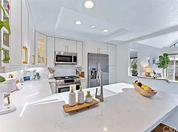 Kitchen with white cabinets, marble countertop, stainless steel appliances, and windows letting in light