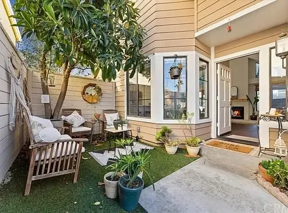 Patio with wooden chairs, cushions, potted plants, and open door to interior with fireplace