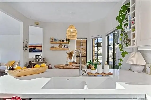 Kitchen with white countertop, sink, plants, wooden bowl with lemons, and dining area visible