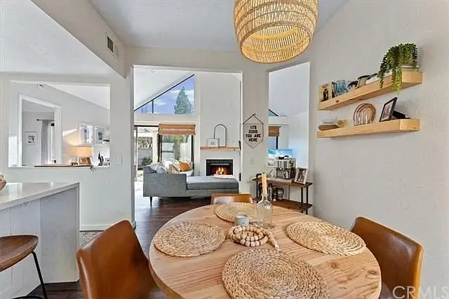 Dining area with round wooden table, chairs, fireplace, shelves, and plants