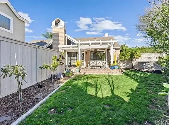 Backyard with lawn, trees, patio with covered seating, and house visible