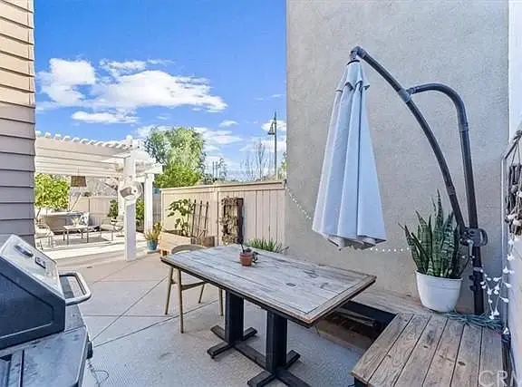 Patio with wooden table, umbrella, barbecue grill, potted plants, and pergola