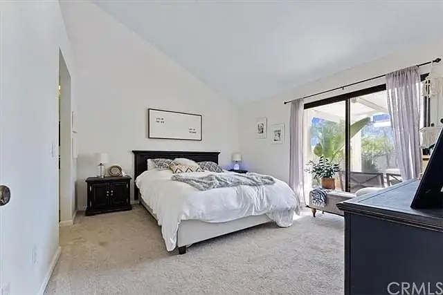 Bedroom with large bed, gray and white bedding, nightstand, and sliding doors to patio