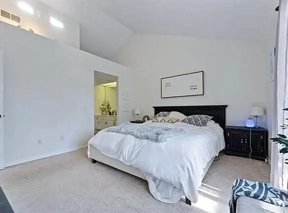 Bedroom with large bed, white bedding, dark dresser, wall pictures, and chair