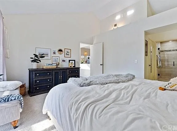Bedroom with large bed, white bedding, dark dresser, wall pictures, and chair
