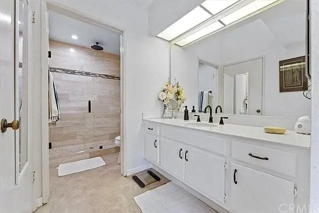 Bathroom with double sink vanity, large mirror, glass-door shower, and tile floor