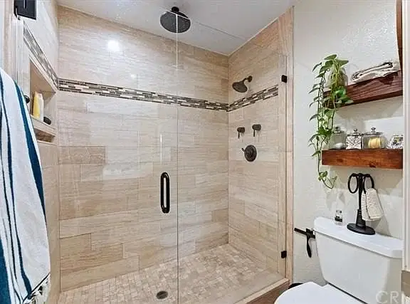 Shower with glass doors, tile walls, two showerheads, shelf, and toilet