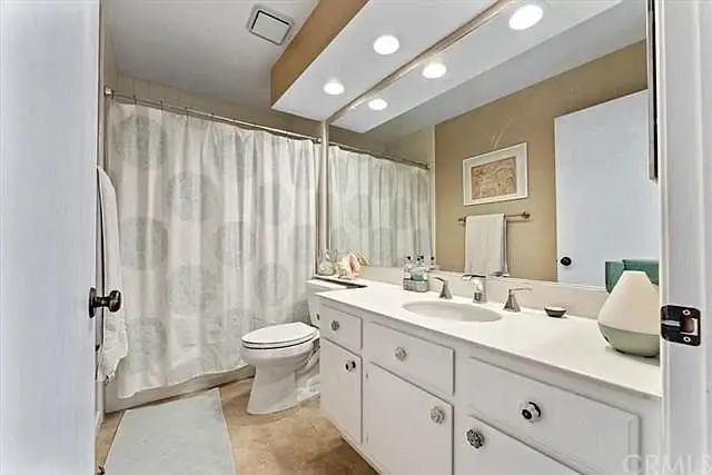 Bathroom with white dual sink vanity, large mirror, toilet, and shower curtain