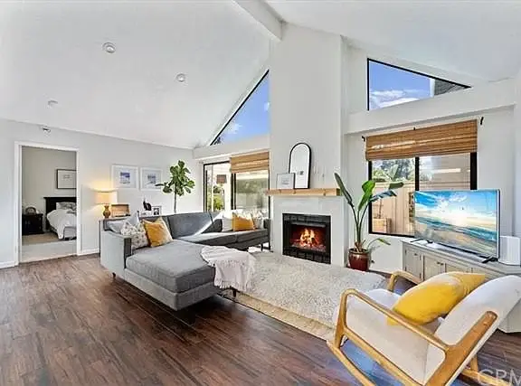 Living room with gray sectional sofa, fireplace, TV, plants, and wood flooring