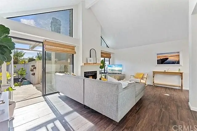 Living room with gray sofa, TV, table with chairs, wooden floor, and indoor plants