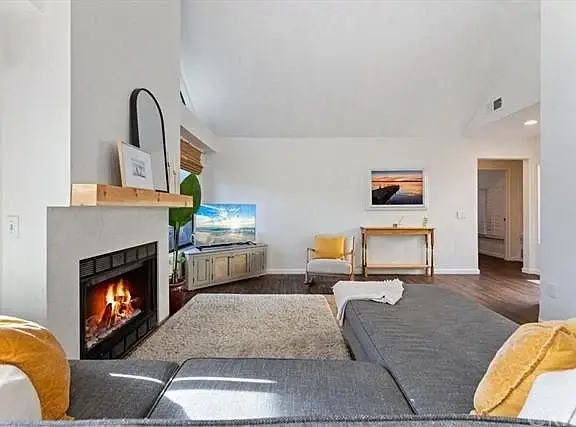 Living room with gray sectional sofa, yellow pillows, fireplace, TV, and rug