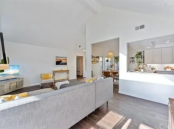 Living room with gray sofa, TV, and open kitchen with light cabinets