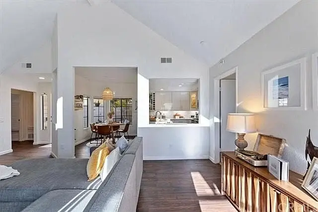 Living room with gray sofa, side table, dining area, and kitchen with white cabinets visible