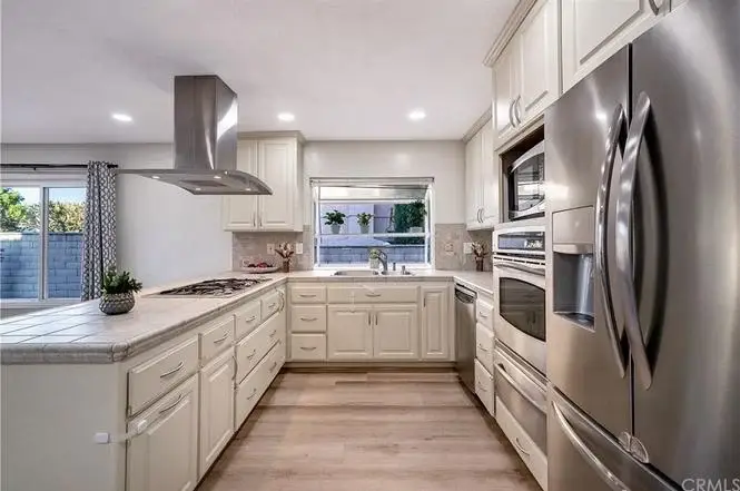 Kitchen with white cabinets, stainless steel appliances, large window, and tiled countertop