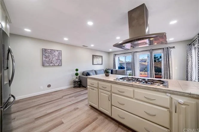 Kitchen with island and cooktop, stainless steel appliances, wooden floors, and living area with windows