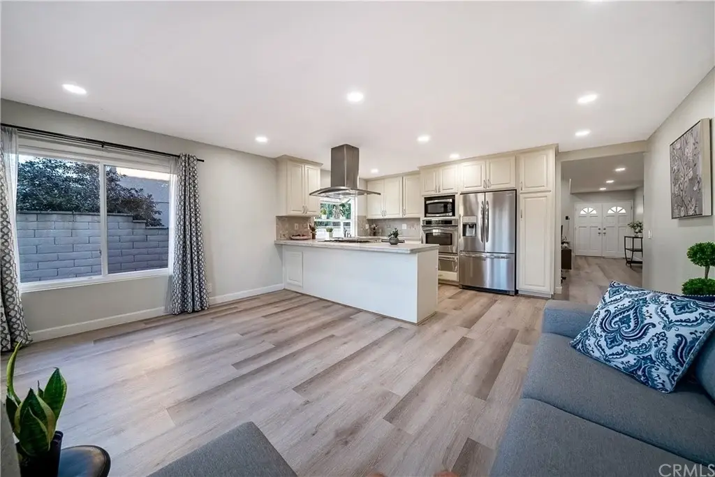 living area with white cabinets, stainless steel appliances, sofa, and light wood floors