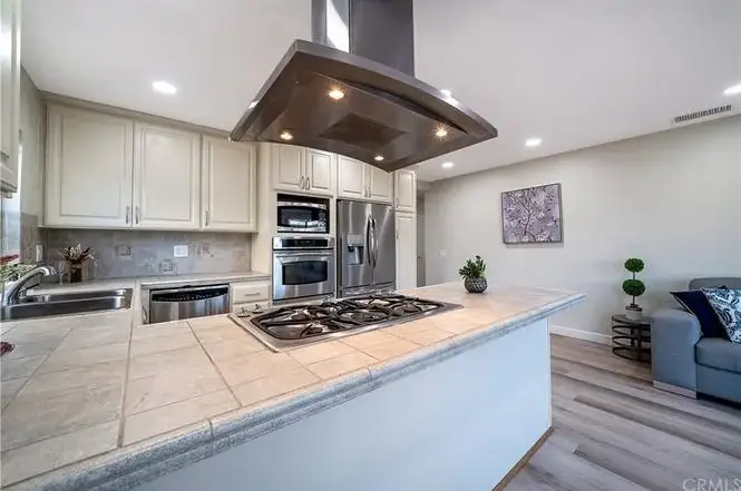 Open-concept kitchen and living area with white cabinets, stainless steel appliances, gray sofa, and light wood floors