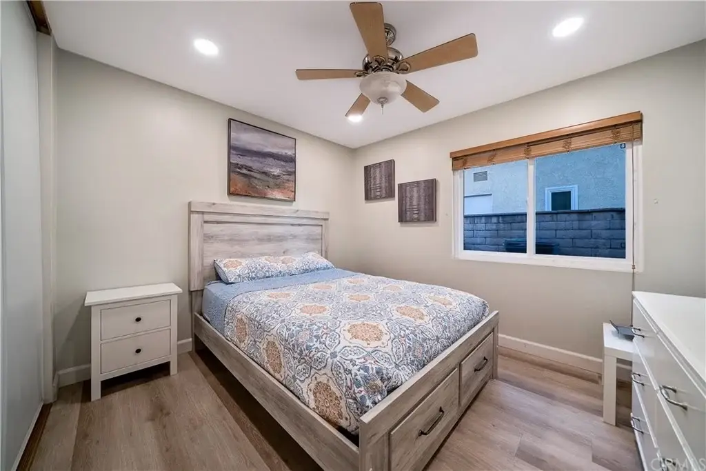 Bedroom with wood bed frame, blue and beige blanket, bedside tables, ceiling fan, and window view