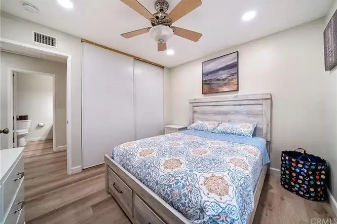 Bedroom with bed, blue and orange blanket, ceiling fan, dresser, closet, and bathroom door