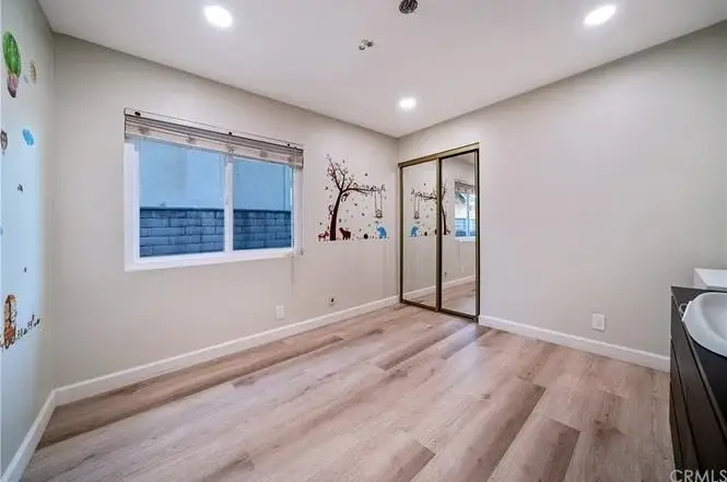 Room with wooden floor, large window with blinds, mirrored closet, and colorful tree wall graphics