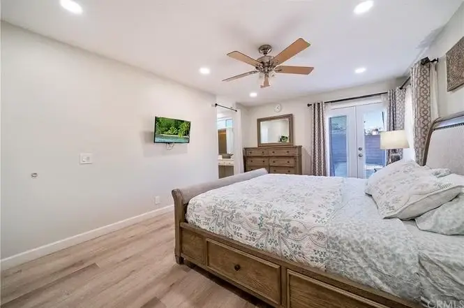 Bedroom with wooden bed, light bedding, ceiling fan, TV, dresser, and sliding glass doors to outdoor area