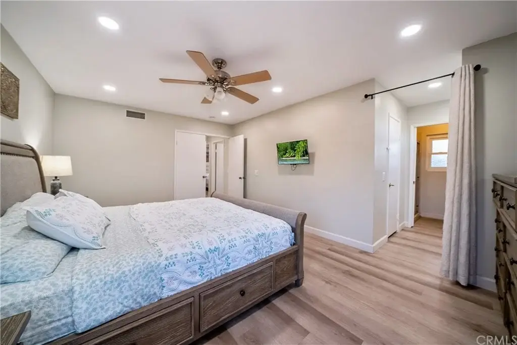 Bedroom with large bed, light bedding, ceiling fan, wooden floor, TV, and doorway to another room