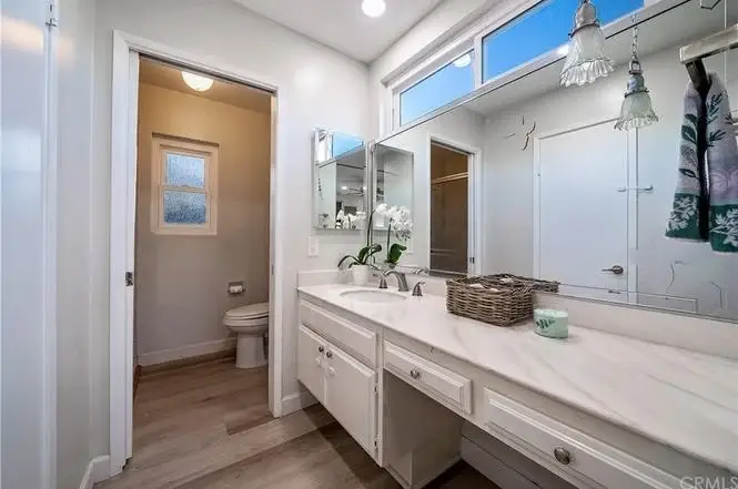 Bathroom with double sink vanity, large mirror, small window, and doorway to toilet area