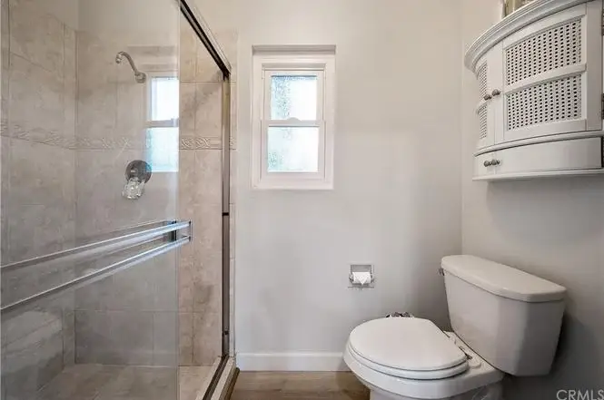 Bathroom with walk-in shower, glass doors, white toilet, and light-colored walls