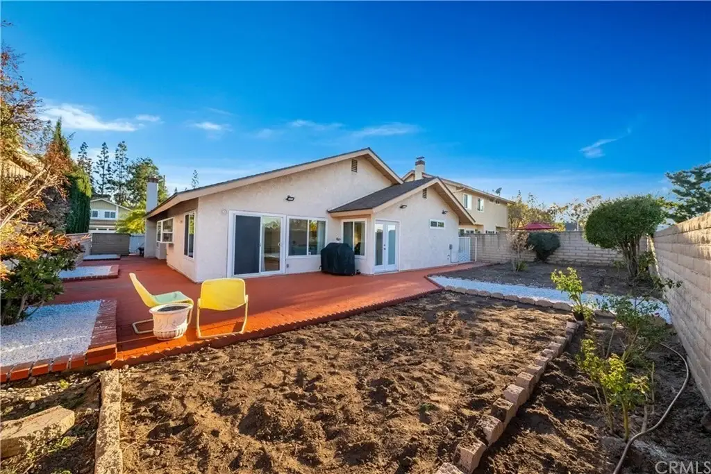 Backyard with patio, two yellow chairs, trees, and shrubs