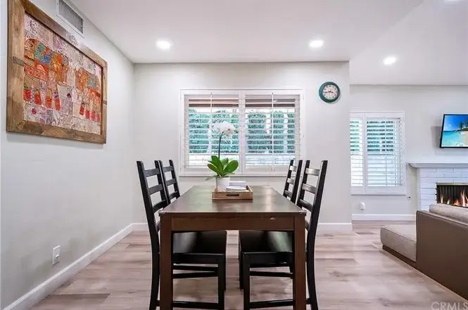 Dining area with wooden table, four chairs, orchid plant, artwork, clock, and fireplace