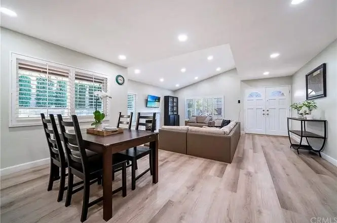 Living and dining area with wood table, chairs, couch, and large windows with blinds