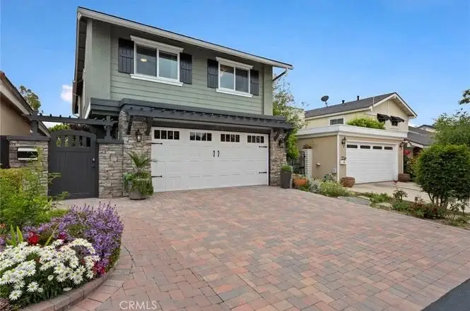Two story house California real estate with gray exterior, stone wall, double garage, brick driveway, and flowers.